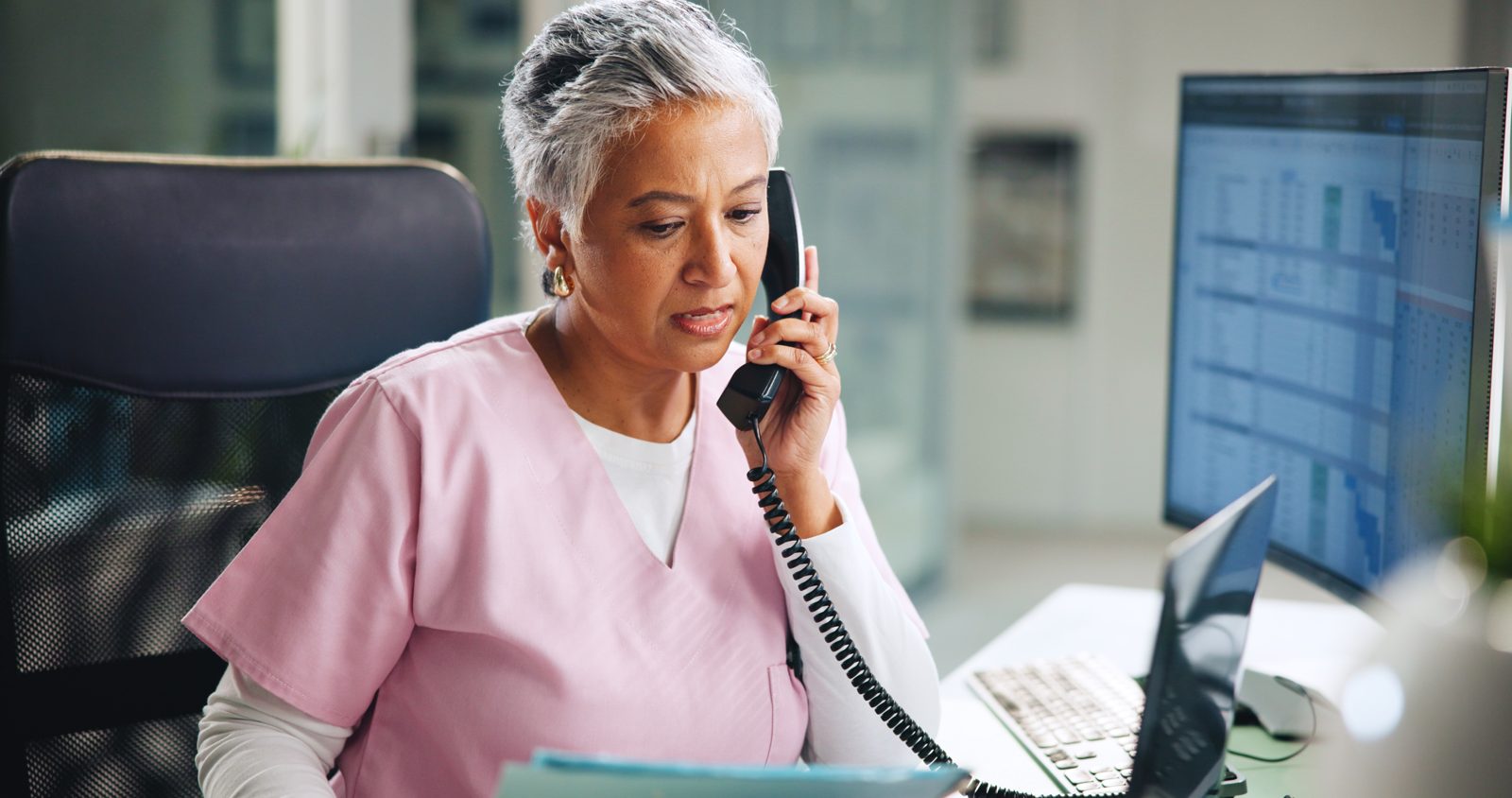 Front desk staff member on the phone while reviewing a chart.