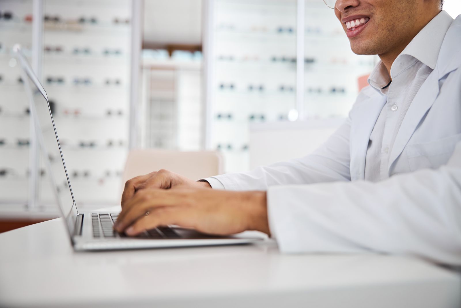 Optometrist smiling while typing on a laptop in an optical shop.
