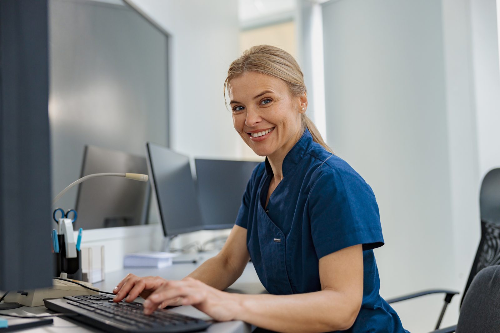 Surgery coordinator smiling while typing at her desk.